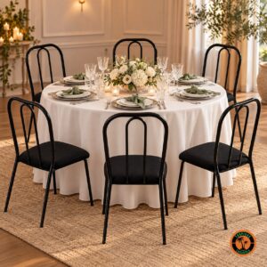 Seis cadeiras tubulares pretas em volta de uma mesa redonda com toalha branca, posta para jantar, com flores brancas