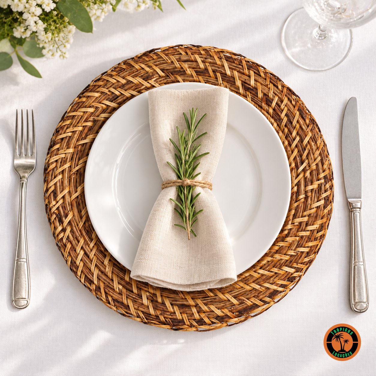 Sousplat de rattan antigo sob prato branco com guardanapo de linho e alecrim