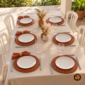 Mesa com sousplats de rattan envernizado, guardanapos terracota e cadeiras plásticas brancas