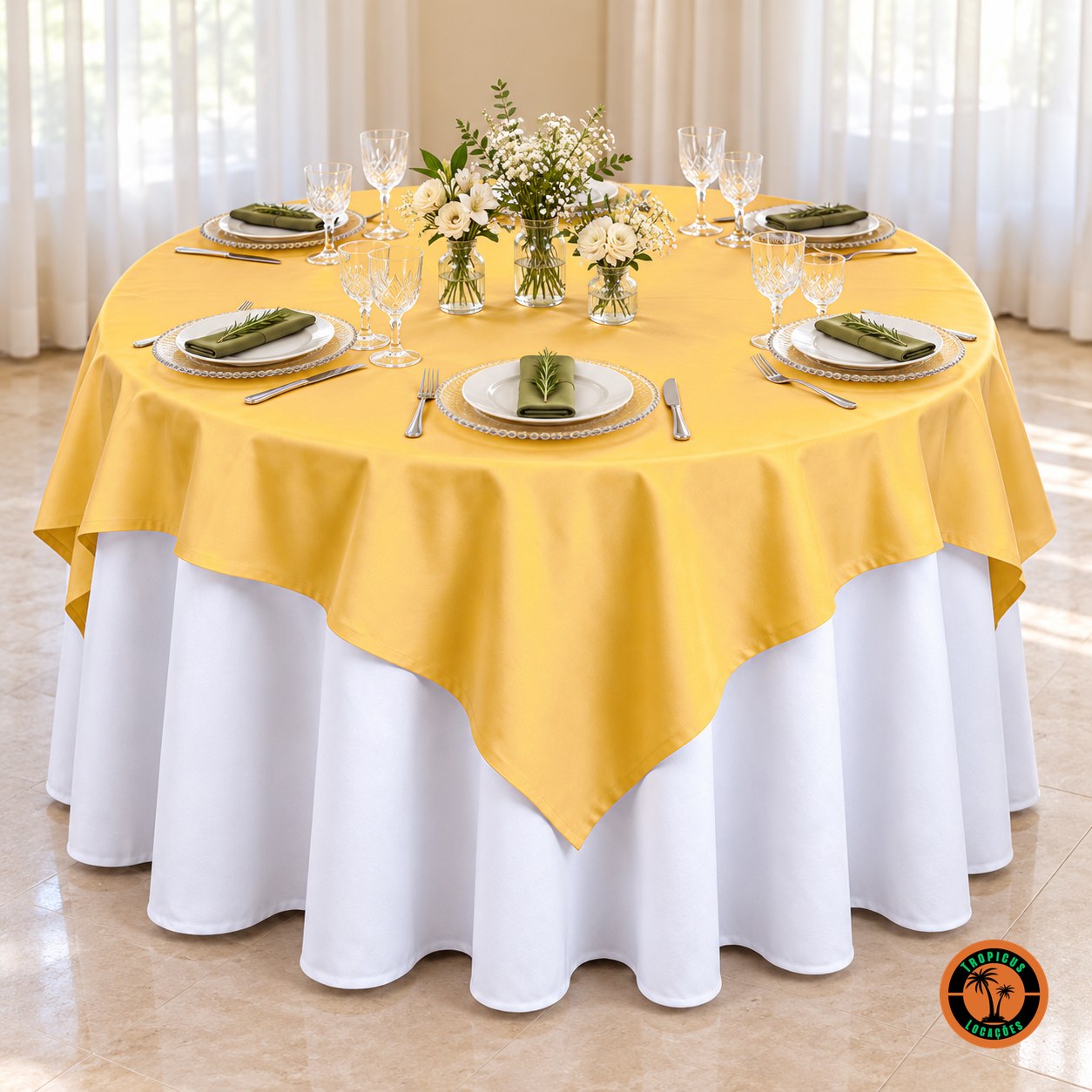 Mesa redonda com cobre-mancha amarelo-ouro sobre toalha branca, sousplats de vidro e flores brancas