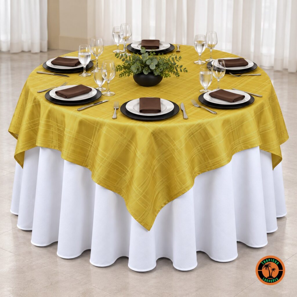 Mesa redonda com cobre-mancha dourado xadrez sobre toalha branca, sousplats pretos e guardanapos marrons
