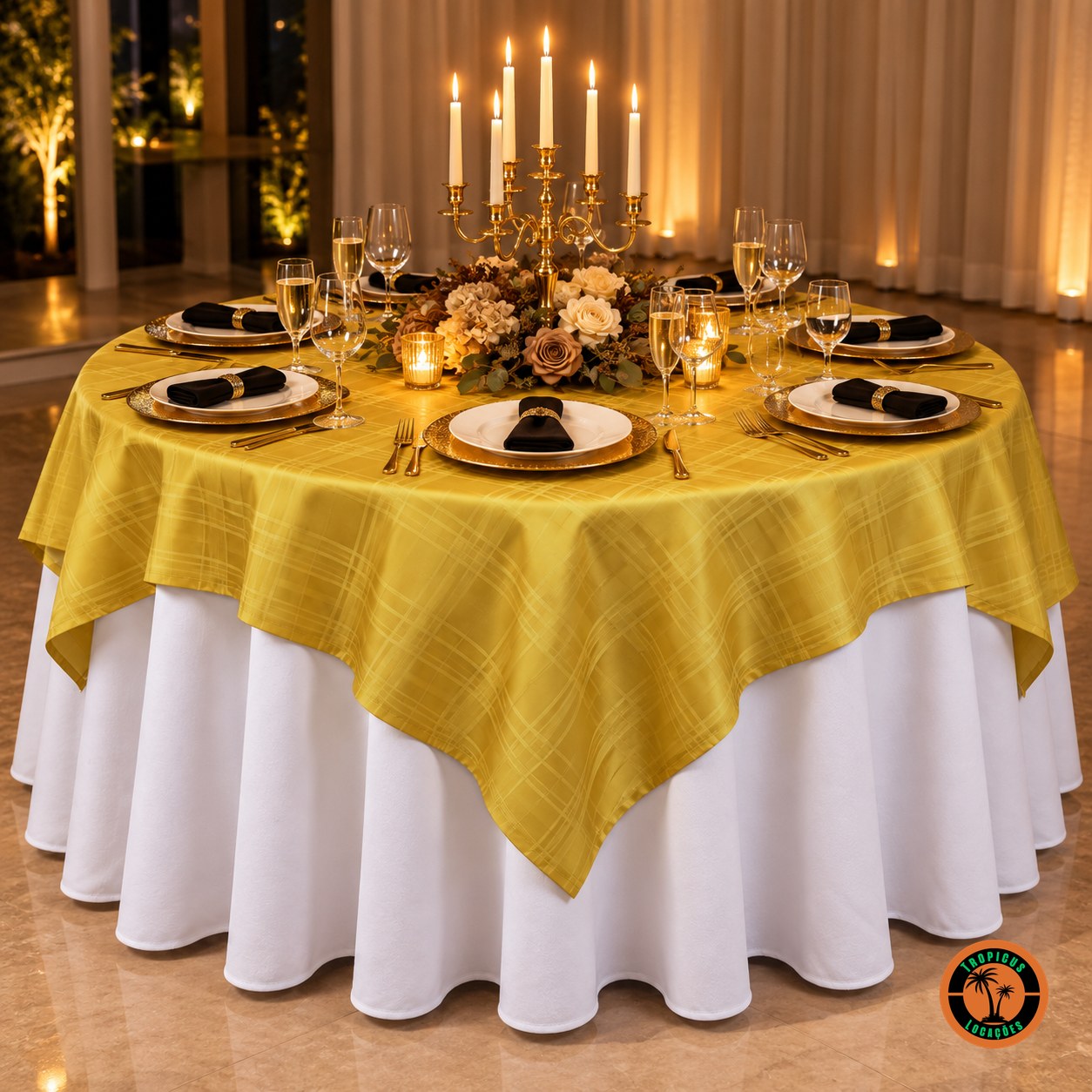 Mesa redonda com cobre-mancha dourado xadrez sobre toalha branca, candelabro dourado com velas