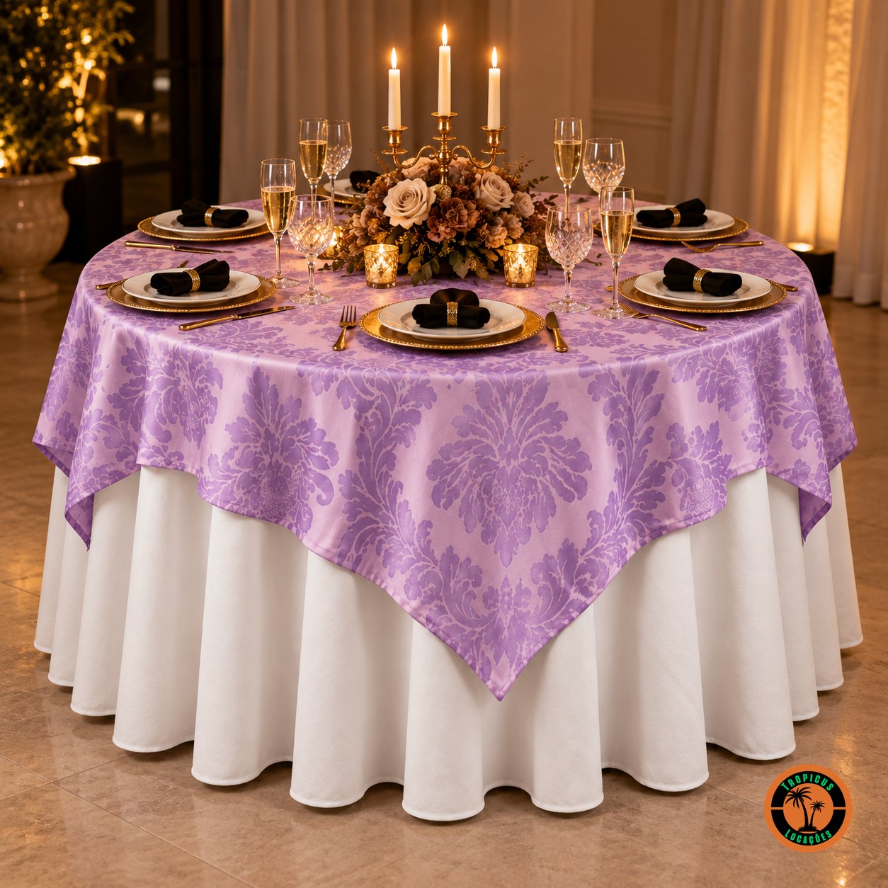 Mesa redonda com cobre-mancha lilás adamascado sobre toalha branca, candelabro com velas